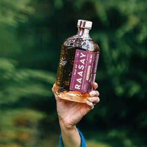 Hand holding Raasay Isle of Raasay Hebridean Single Malt Scotch Whisky bottle against green foliage