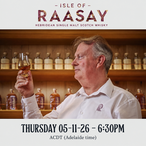 Alasdair Day with a dram to taste, set against a background of wooden shelves filled with bottles.