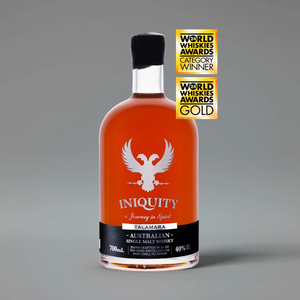 A bottle of Iniquity Talamara single malt whisky with amber liquid, a silver double headed pheonix logo, and a black label, shown on a gray background with two gold World Whiskies Awards badges.